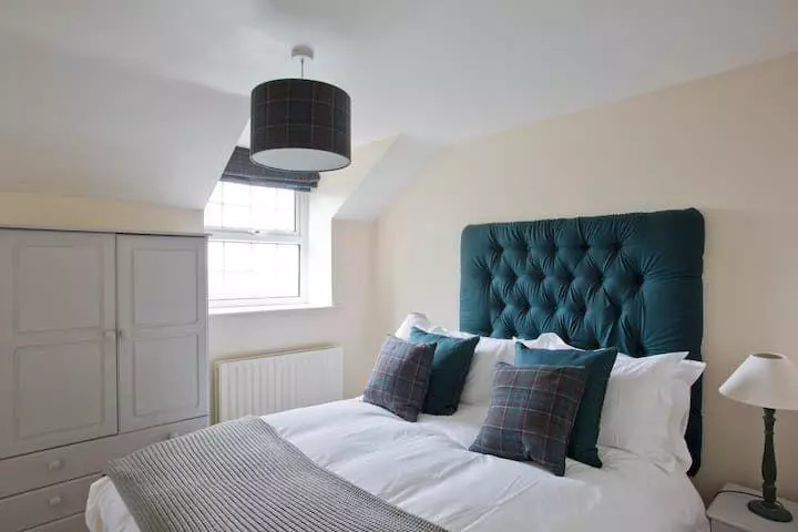 Main bedroom with teal headboard and tartan cushions